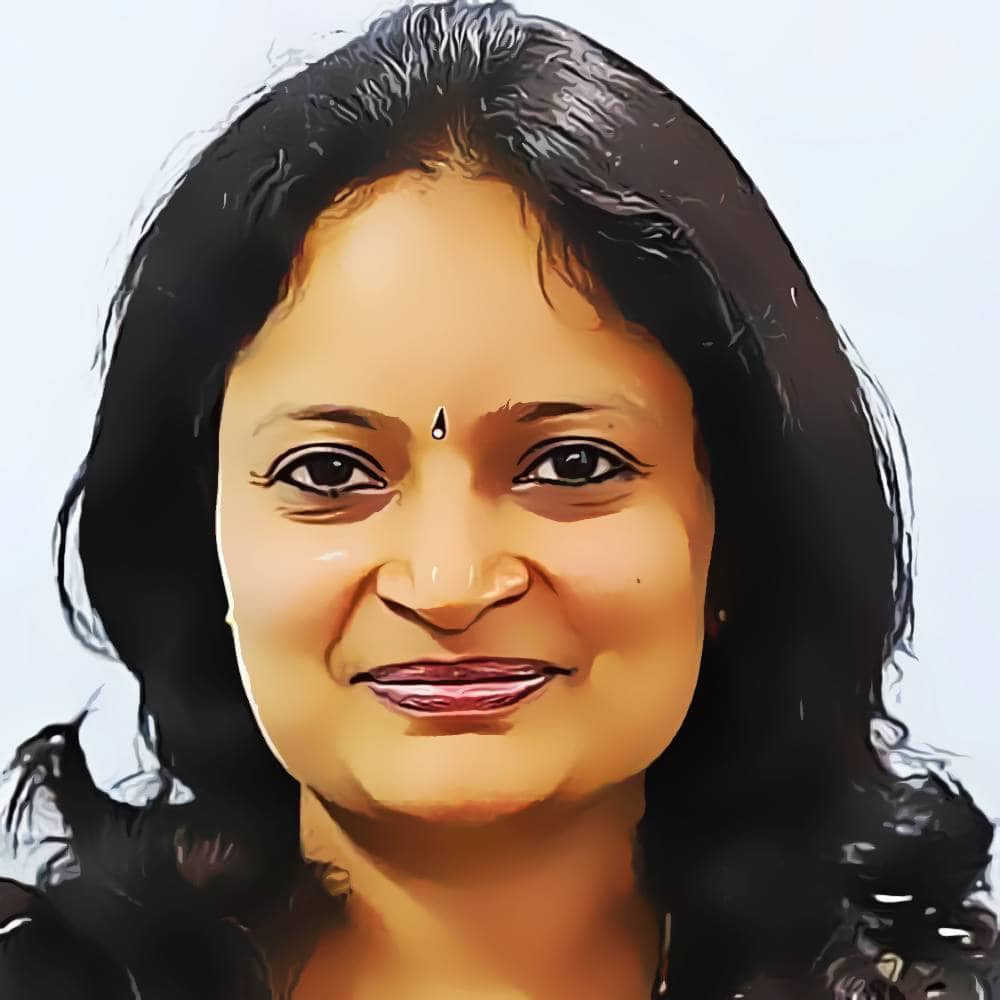 Portrait of a smiling woman with long hair, wearing a small bindi on her forehead, against a light background, representing wellbeing and Ayurvedic health.